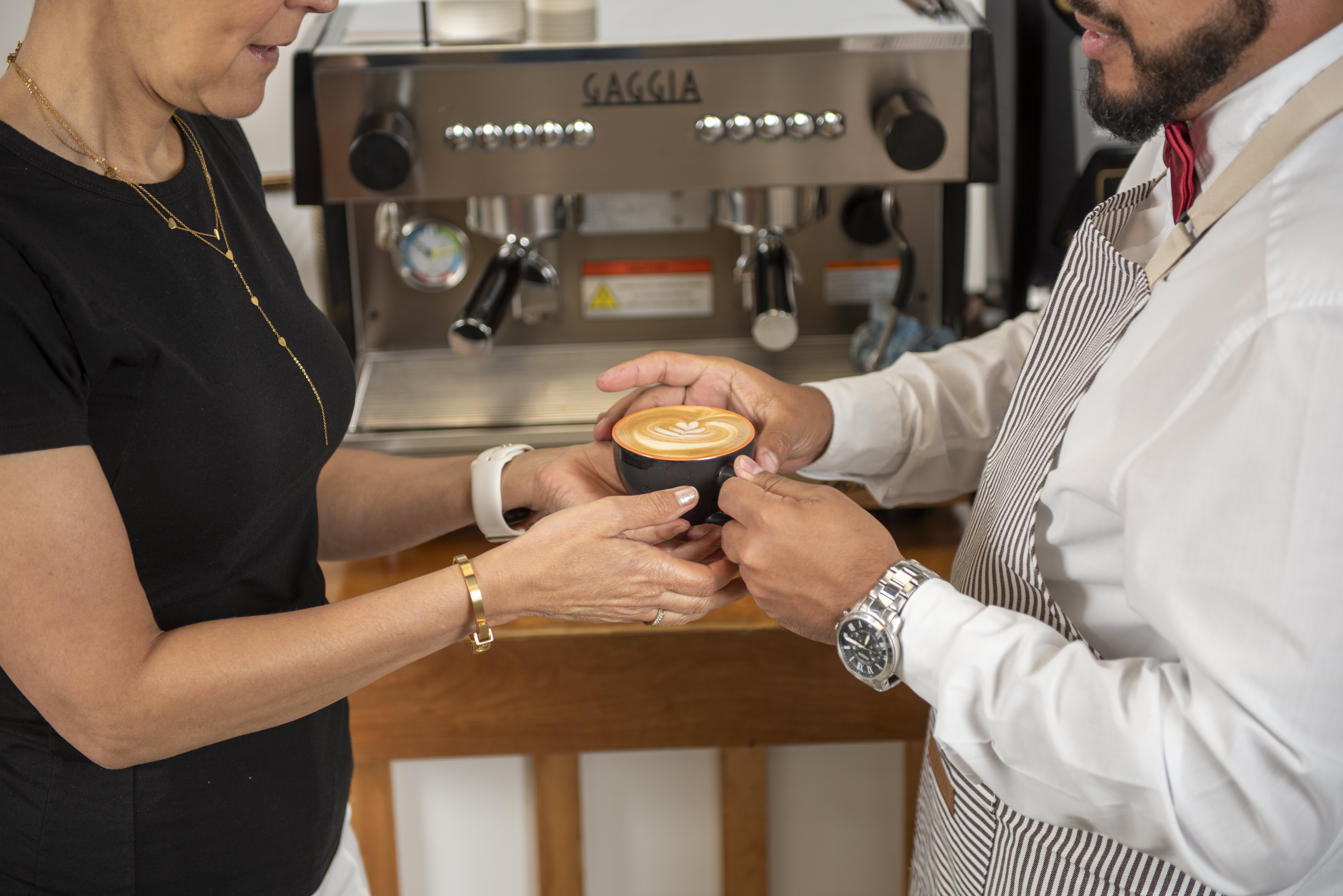 Professional barista delivering premium coffee with latte art to elegant client