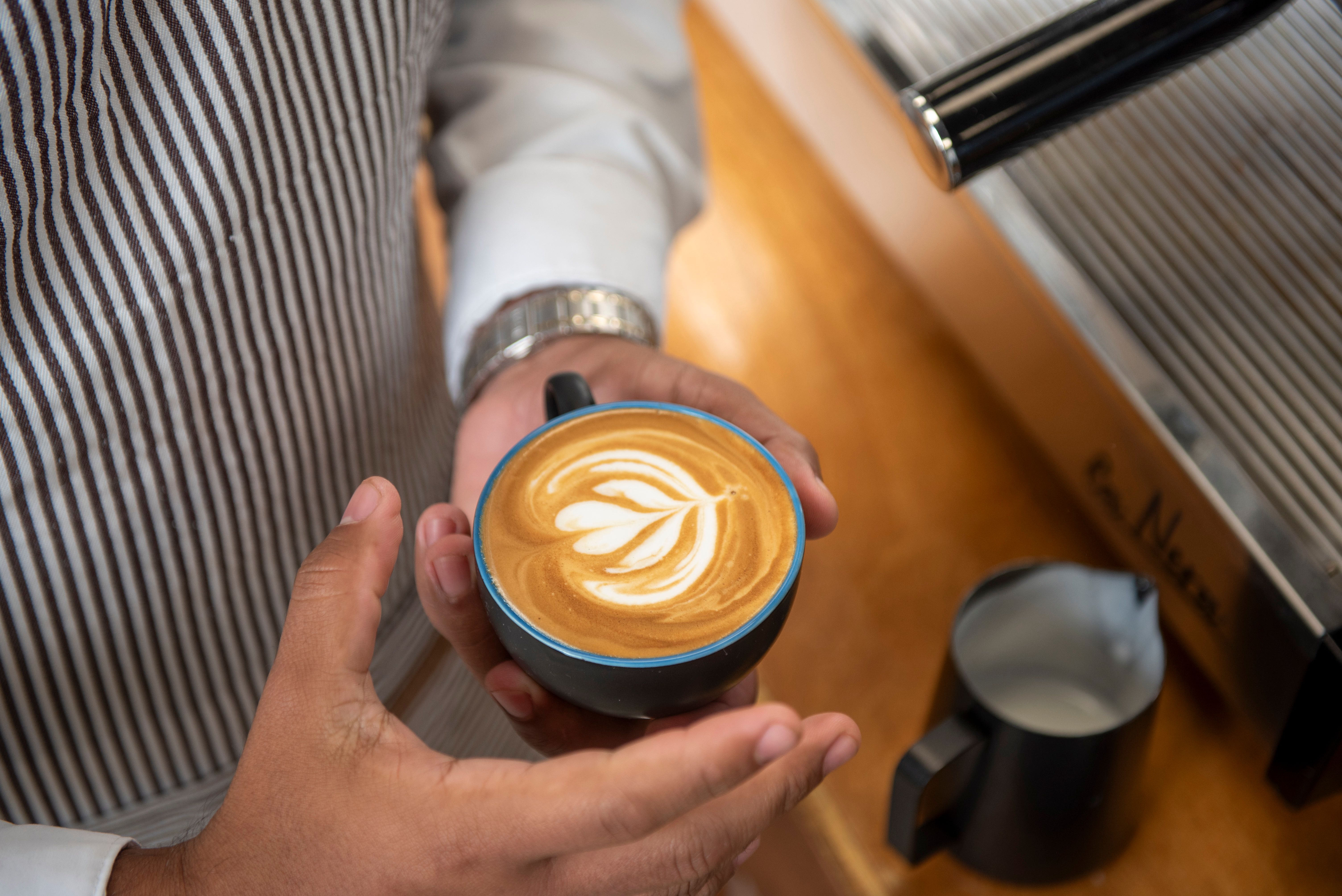 Expert barista hands holding perfect latte art coffee